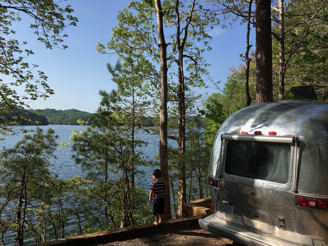Boy looking at lake beside Airstream